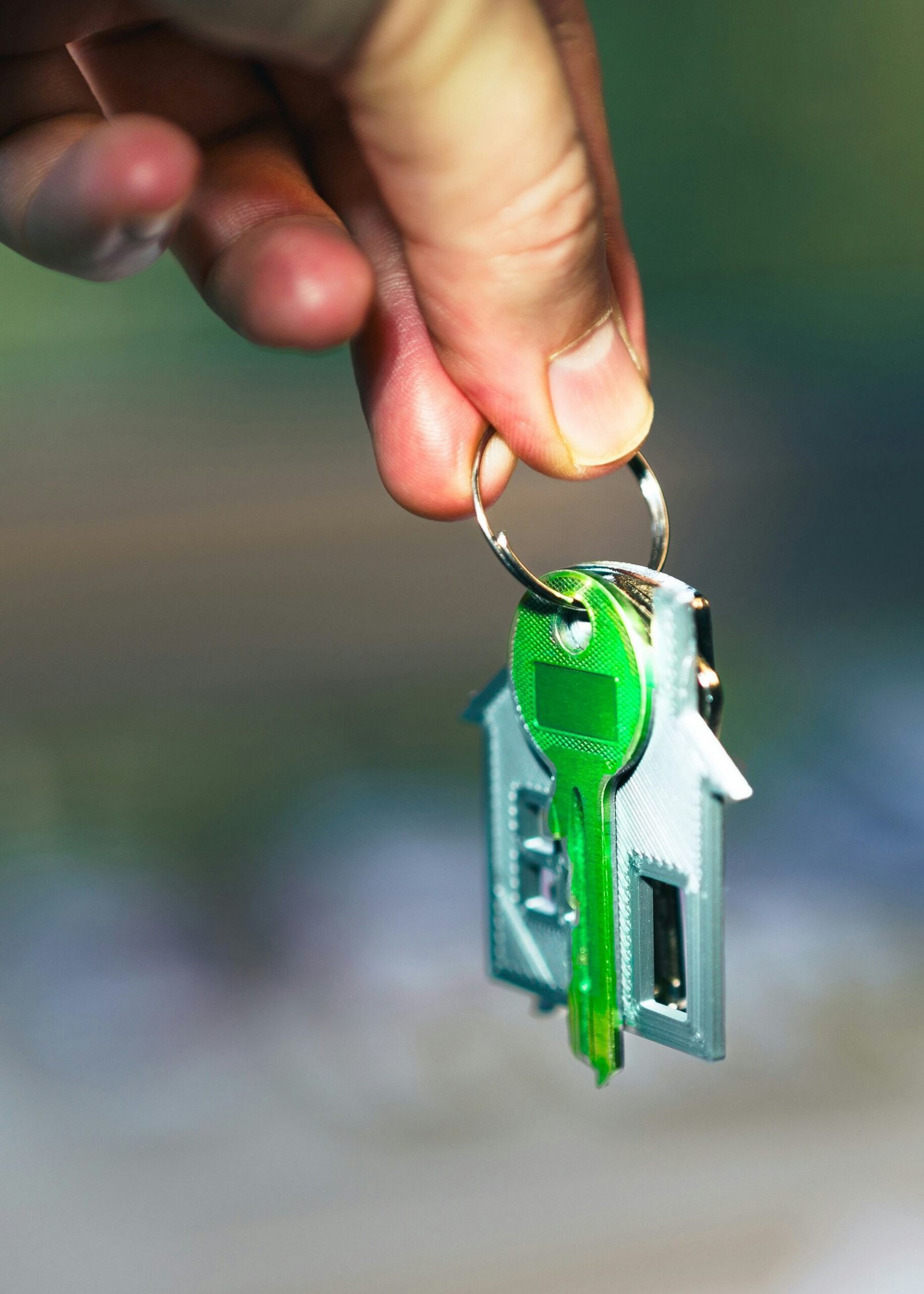 A hand holding a green key to a house